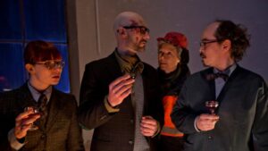 En gruppe mennesker i jakkesæt og briller diskuterer under en Julekalender tv-begivenhed i 2021.